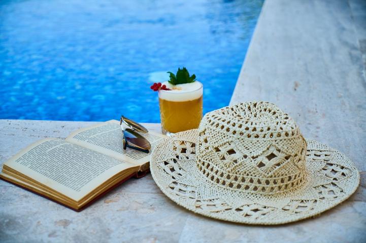 un livre, un chapeu de paille et un cocktail au bord d'une piscine