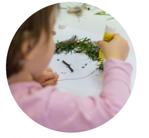 enfant en train de coller des feuilles sur un modèle de visage 